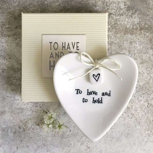 A lovely ceramic heart shaped ring dish with a little bow and square with a little heart printed on it. The dish is presented in a box with a lid. The words To Have and To Hold are written on the box as well as on the little dish.