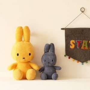 Two corduroy Miffy soft toys sitting by a wall one large yellow one and a smaller dark blue one