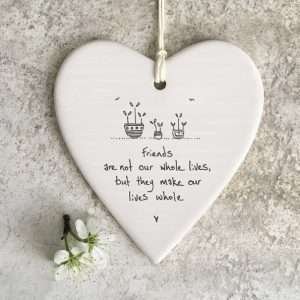 A lovely white ceramic hanging heart with an image of some plants on it and the wording Friends are not our whole lives, but they make our lives whole.