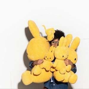 A child holding several Miffy soft toys in yellow corduroy