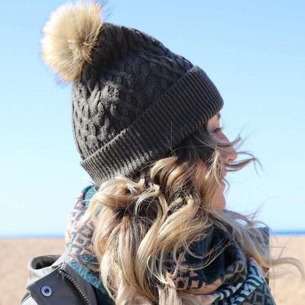 An olive green fleece lined, cable knit bobble hat in wool mix with a natural fuax fur pom pom