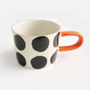 A lovely ceramic mug with an elongated handle and a mono spot design with an orange handle