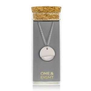 A silver chain necklace with a white porcelain disk pendant dipped in silver in a glass bottle with a cork lid