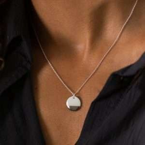 A silver chain necklace with a white porcelain disk pendant dipped in silver worn around a lidies neck