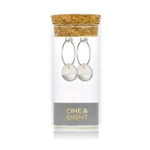 White porcelain disks dipped in silver suspended from silver earring hoops in a glass bottle with a cork lid