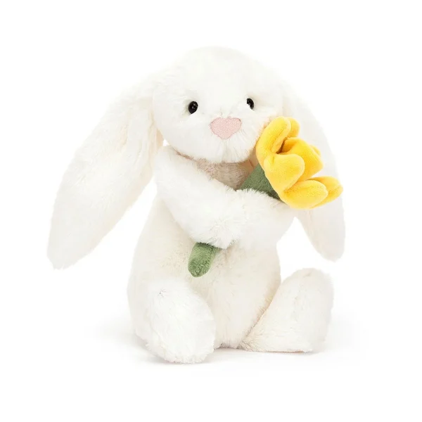 A soft toy from Jellycat a white fluffy bunny with a cute face holding a daffodil