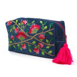 A blue velvet wash bag embroidered with a pink and lime green embroidered desgn. A gold zip fastening has a pink tassel