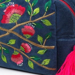 A blue velvet wash bag embroidered with a pink and lime green embroidered desgn. A gold zip fastening has a pink tassel