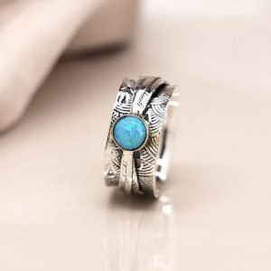 Sterling silver spinning ring with deco embossed detail and a single opal cabochon on a moving leaf band